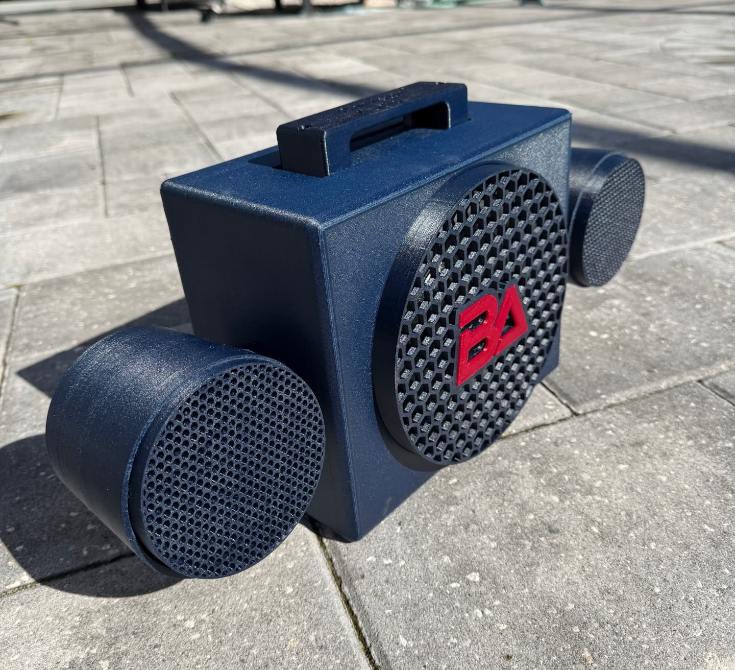 BA Move 1 on a sunlit patio — the embossed carry handle, honeycomb grille with the red BA mark, and both rotating sphere pods